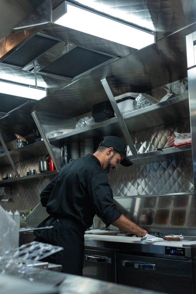 Chef working in a stainless steel modern food truck kitchen, preparing a dish with focus and precision.